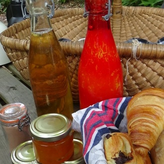 Petit déjeuner champêtre avec jus de pomme, confitures, miel et panier de croissants, pains au chocolat et petits pains